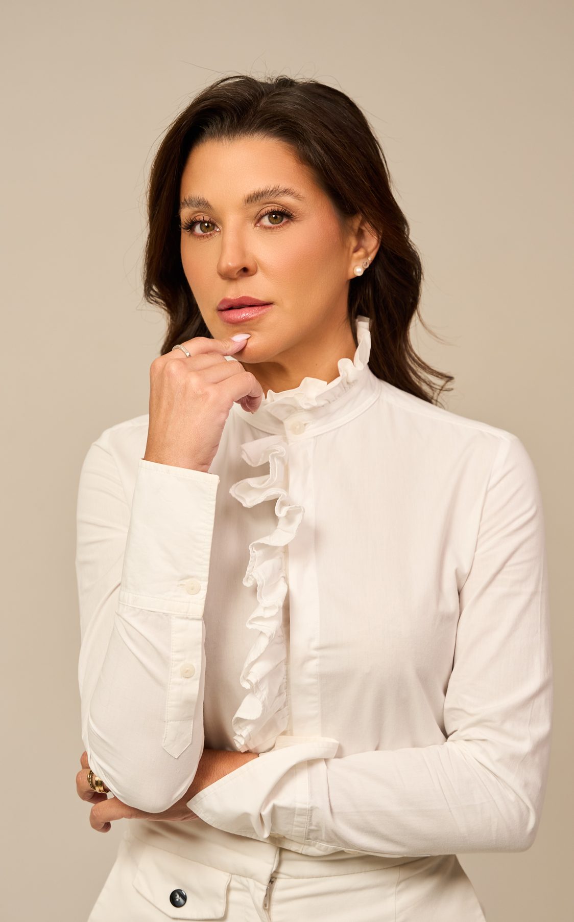 Dra. Carolina Rosa de camisa branca com babados, com a mão no queixo