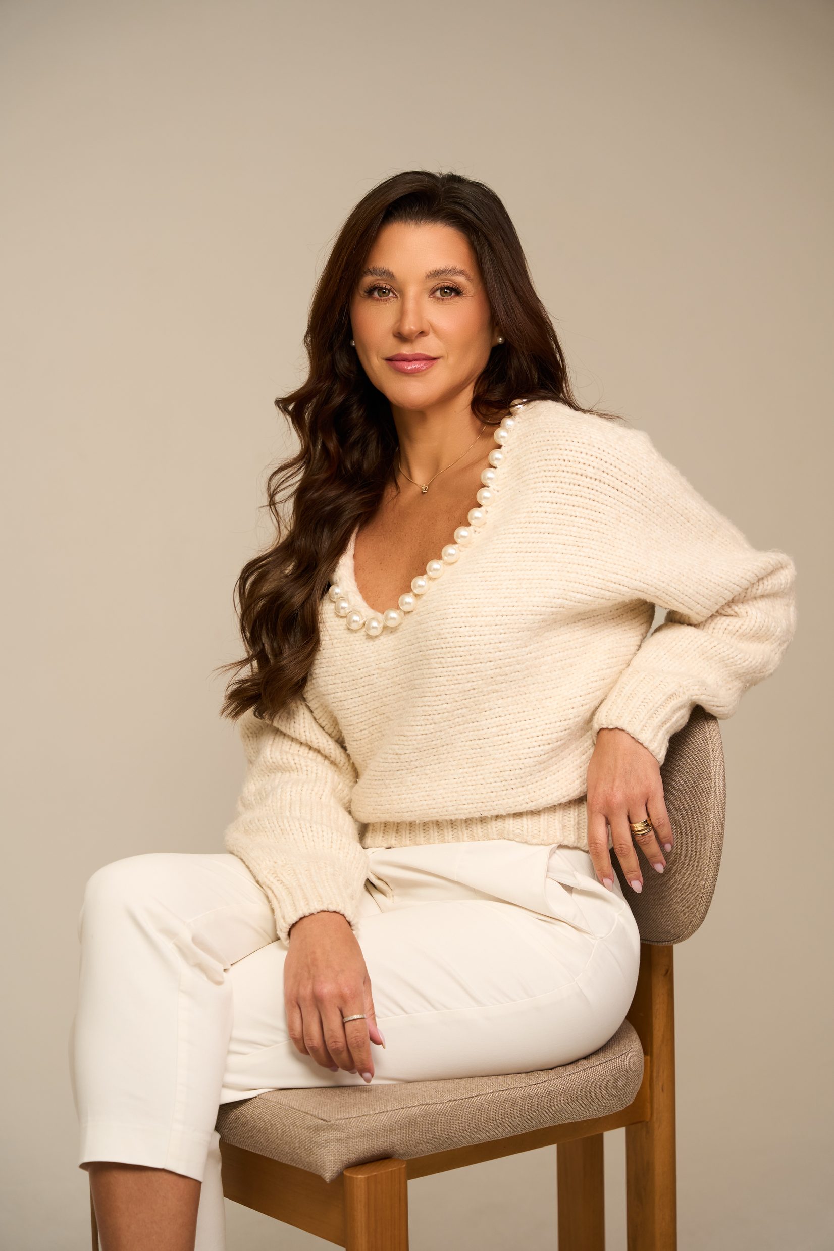 Dra. Carolina Rosa sentada, com suéter claro e colar de pérolas