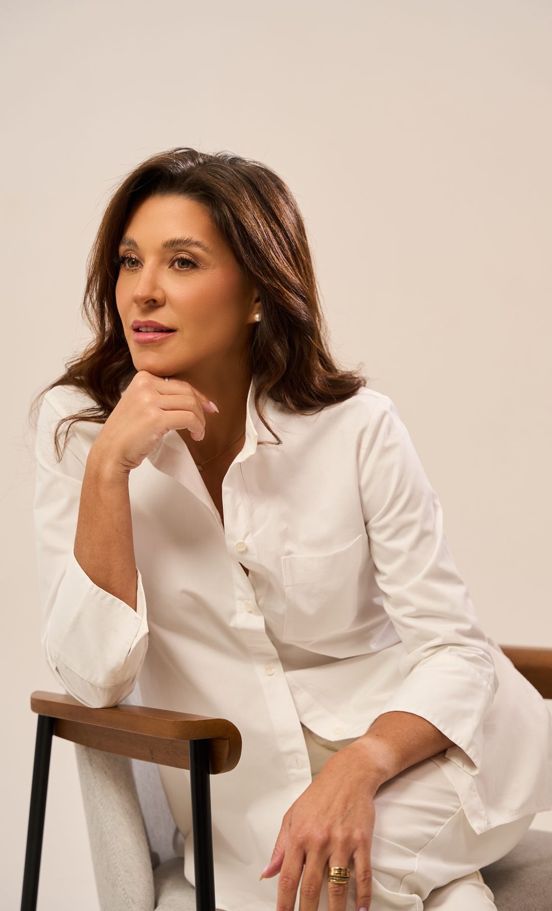 Dra. Carolina Rosa sentada em uma cadeira de madeira, com camisa branca e a mão no queixo
